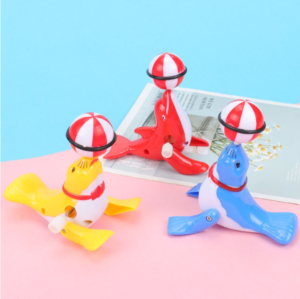Colorful wind-up sea lion toys in red, blue, and yellow balancing striped balls on their noses